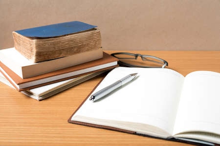 open notebook with stack of book on wood backgroundの写真素材