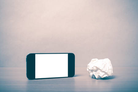 smart phone and crumpled paper on wood background vintage style