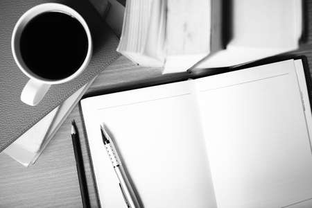 open notebook with book and coffee cup on wood black and white color tone styleの写真素材