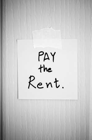 sticky note write a message pay the rent on wood door background black and white color tone styleの写真素材