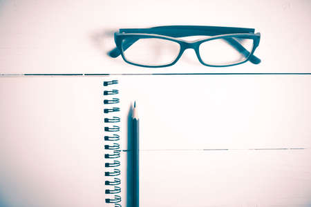 pencil and notepad with eyeglasses over white table view from above vintage styleの写真素材