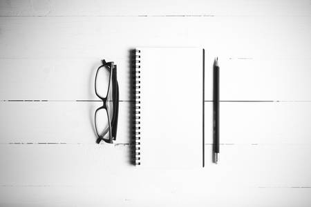 pencil and notepad with eyeglasses over white table view from above black and white color style