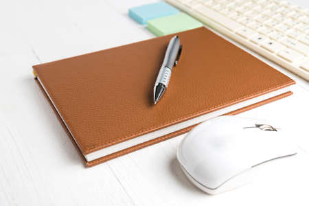 computer and brown notebook with office supplies on white tableの写真素材
