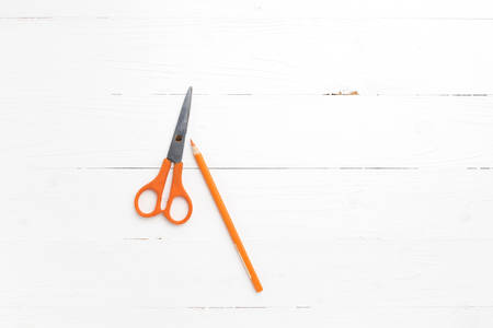 orange scissors and pencil on white tableの写真素材