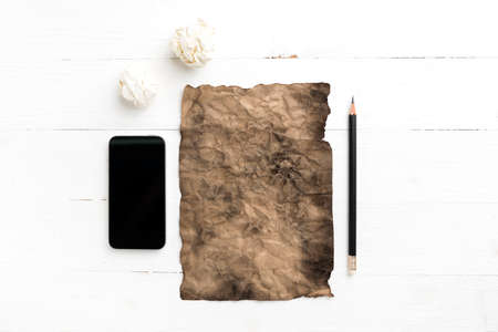 burning brown paper and crumpled paper with smart phone over white tableの写真素材