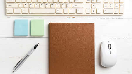 computer and brown notebook with office supplies on white tableの写真素材