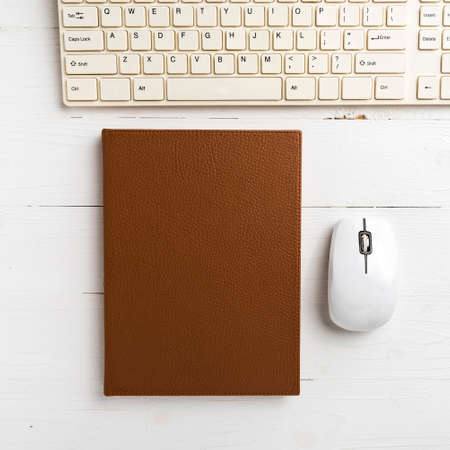 computer and brown notebook with office supplies on white tableの写真素材