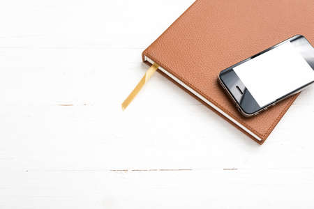 cellphone on notebook over white tableの写真素材