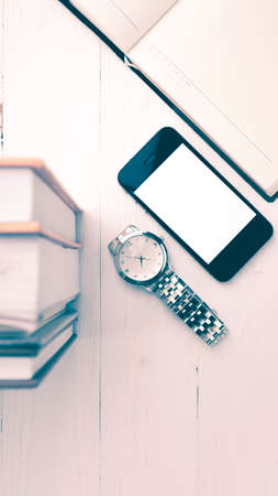 cellphone with stack of book and watch over white table vintage style