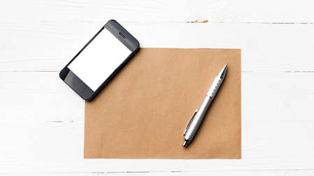 cellphone with brown paper and pen over white tableの写真素材