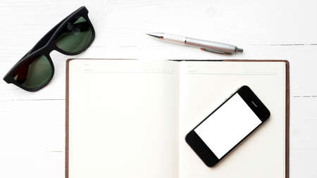 cellphone with notebook and sunglasses over white table