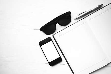 cellphone with notebook and sunglasses over white table black and white color styleの写真素材