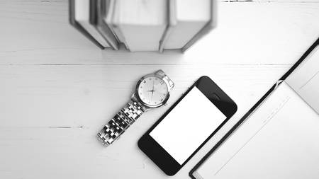 cellphone with stack of book and watch over white table black and white tone color styleの写真素材