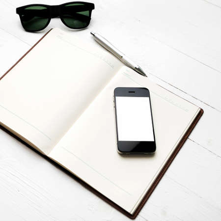 cellphone with notebook and sunglasses over white tableの写真素材