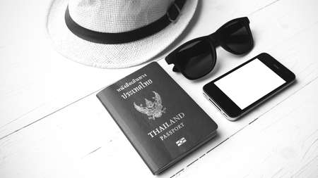 hat sunglasses smart phone and passport over white table black and white color