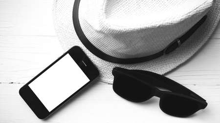 hat sunglasses and smart phone on white table black and white colorの写真素材