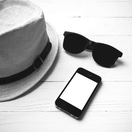 hat sunglasses and smart phone on white table black and white color