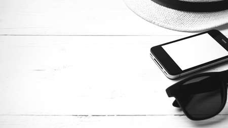 hat sunglasses and smart phone on white table black and white colorの写真素材