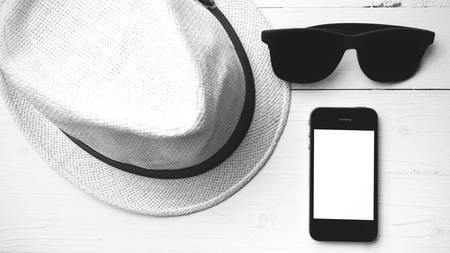hat sunglasses and smart phone on white table black and white colorの写真素材