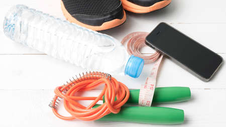 fitness equipment : running shoes,jumping rope,drinking water,measuring tape and phone on white wood...