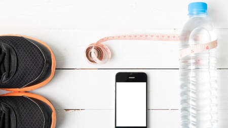 fitness equipment : running shoes,drinking water,measuring tape and phone on white wood tableの写真素材