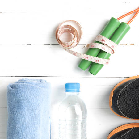 fitness equipment : running shoes,towel,jumping rope,water bottle and measuring tape on white wood...