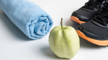 fitness equipment : running shoes,blue towel and guava fruit on white wood table