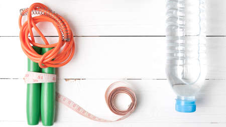 fitness equipment : jumping rope,measuring tape and water bottle on white wood table