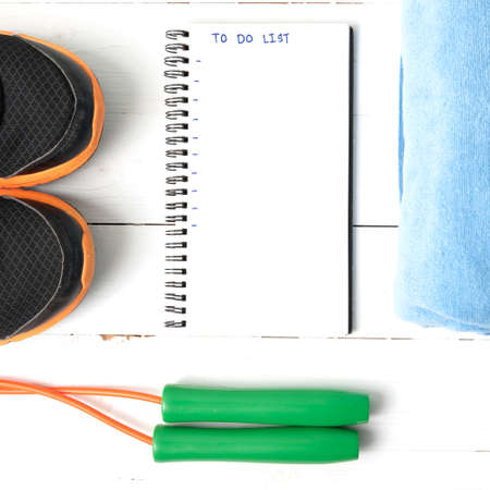 fitness equipment : running shoes,towel,jumping rope and notebook write to do list on white wood...