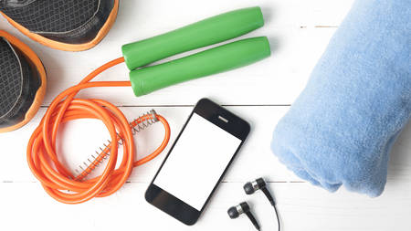 fitness equipment : running shoes,towel,jumping rope and phone on white wood table