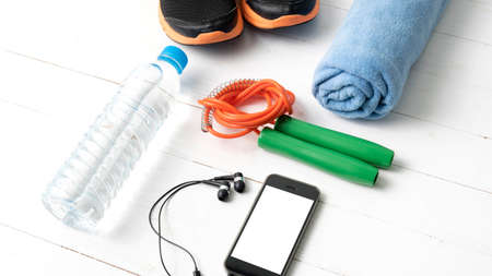 fitness equipment : running shoes,towel,jumping rope,water bottle and phone on white wood table