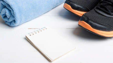 fitness equipment : running shoes,blue towel and notepad on white wood table