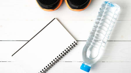fitness equipment : running shoes,drinking water and notebook on white wood tableの写真素材