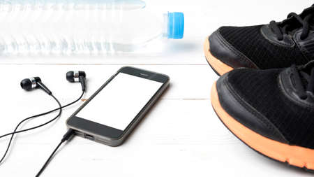 fitness equipment : running shoes,drinking water and phone on white wood table