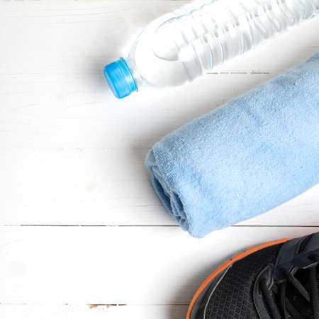 fitness equipment:blue towel,drinking water and running shoes on white wood table