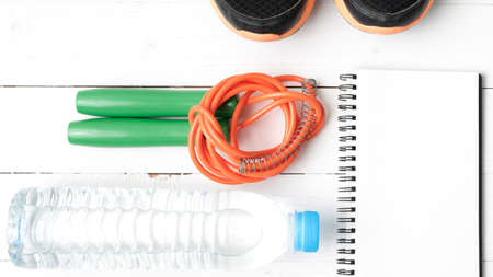 fitness equipment : running shoes,jumping rope,drinking water and notepad on white wood tableの写真素材