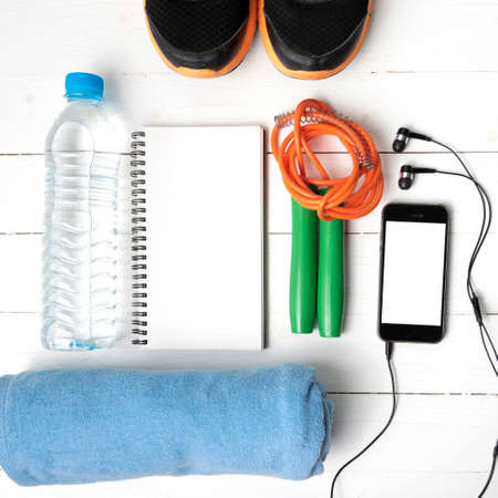 fitness equipment : running shoes,towel,jumping rope,water bottle,phone and notepad on white wood tableの写真素材