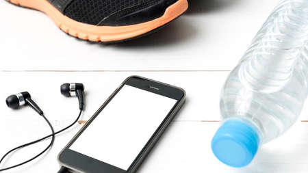 fitness equipment : running shoes,drinking water and phone on white wood tableの写真素材