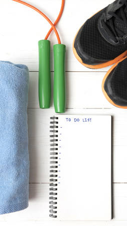 fitness equipment : running shoes,towel,jumping rope and notebook write to do list on white wood tableの写真素材