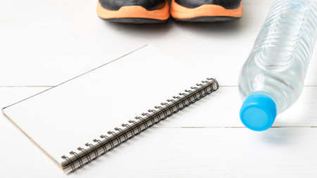 fitness equipment : running shoes,drinking water and notebook on white wood tableの写真素材