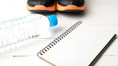 fitness equipment : running shoes,drinking water and notebook on white wood tableの写真素材