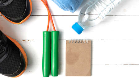fitness equipment : running shoes,towel,jumping rope,water bottle and notepad on white wood table