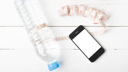 fitness equipment : drinking water,measuring tape and phone on white wood table