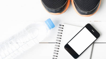 fitness equipment : running shoes,drinking water,notebook and phone on white wood tableの写真素材