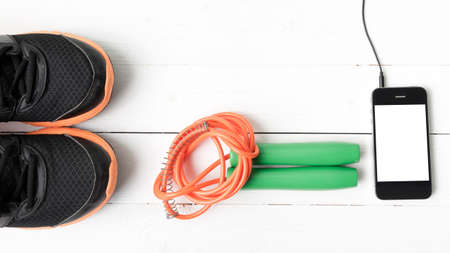 fitness equipment : running shoes,jumping rope and phone on white wood table
