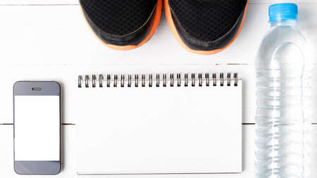 fitness equipment : running shoes,drinking water,notebook and phone on white wood tableの写真素材