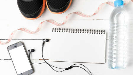 running shoes,measuring tape,drinking water,notebook and phone on white wood tableの写真素材