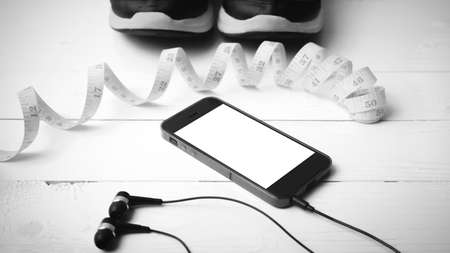 running shoes,measuring tape and phone on white wood table black and white tone color styleの写真素材