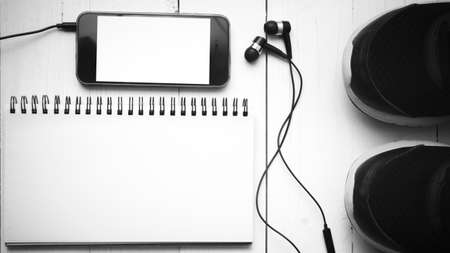 running shoes,notebook and phone on white wood table black and white tone color style