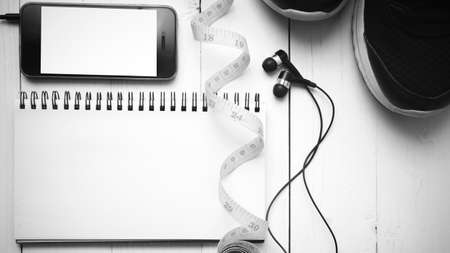 running shoes,measuring tape,notebook and phone on white wood table black and white tone color styleの写真素材